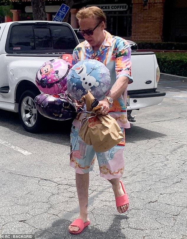 Nicolas Cage, 61, makes the rare move of wearing bright colors with PINK slides as he heads to a birthday party